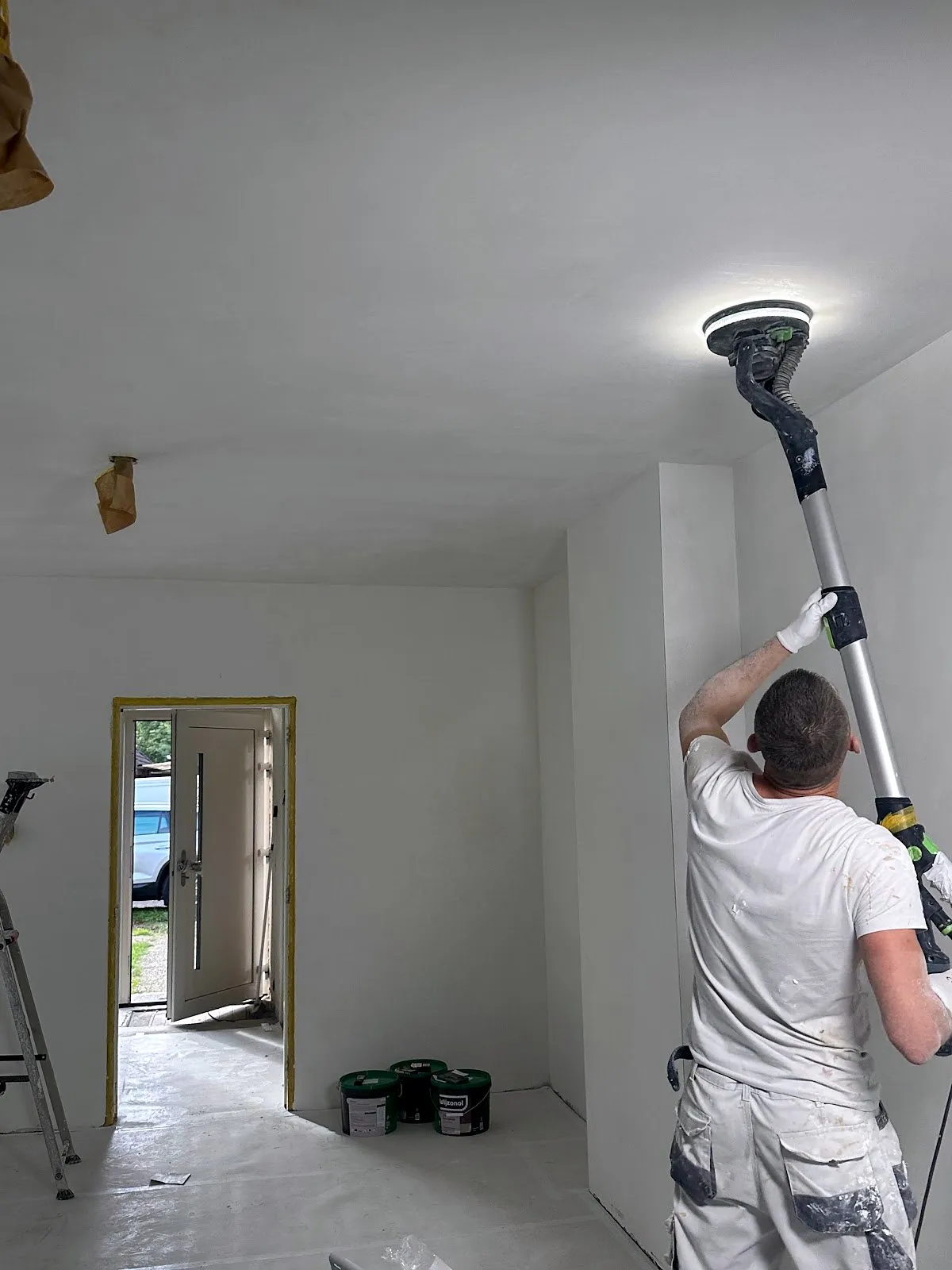 Een gestuct plafond wordt stofarm nageschuurd