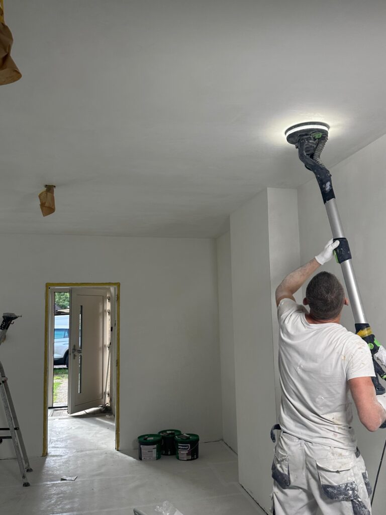 Stukadoor schuurt het plafond met een langnekschuurmachine